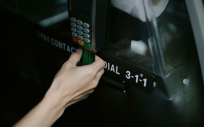 Hand inserting card into ATM, illustrating sneaky scams in a dimly lit setting.