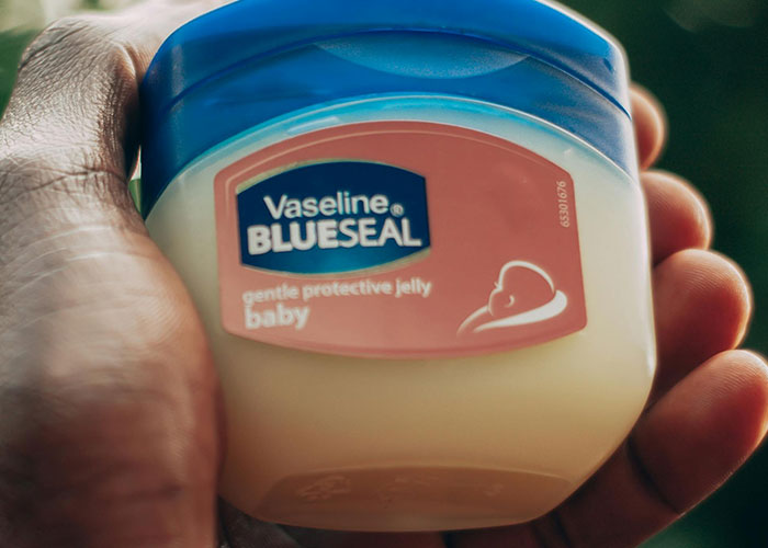 Hand holding a jar of Vaseline Blue Seal, a common beauty tip product for skin care.