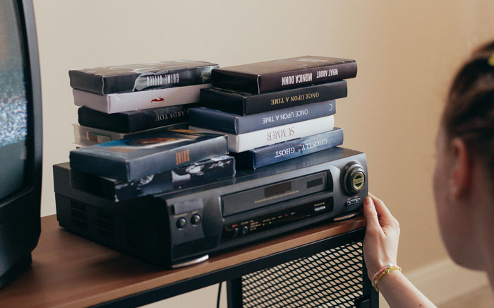 A person placing VHS tapes on a VCR, possibly using it as a hiding spot at home.
