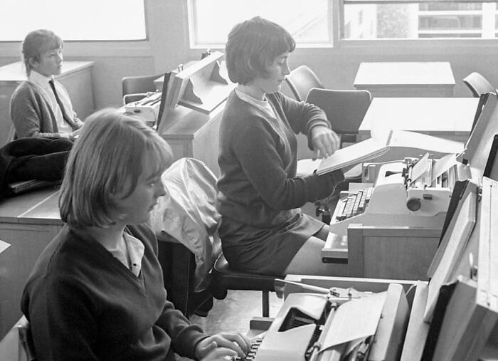 Personas trabajando en máquinas de escribir en una oficina antigua, evocando días pasados.