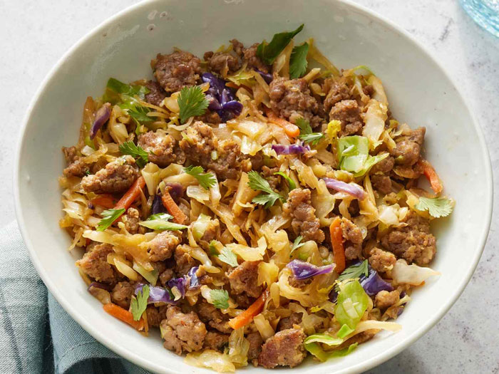 Lazy meal featuring a bowl of stir-fried cabbage with ground meat and colorful vegetables on a light background.
