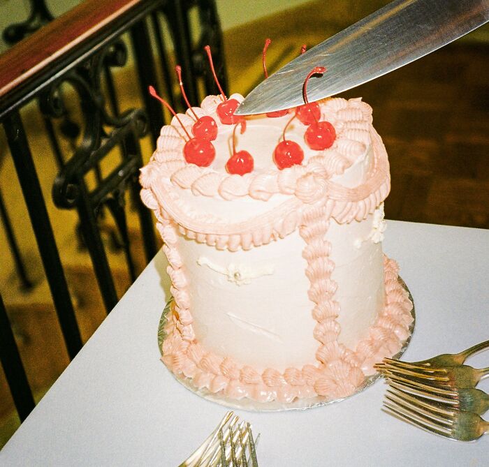 Wedding cake with pink icing and cherries being cut with a large knife.