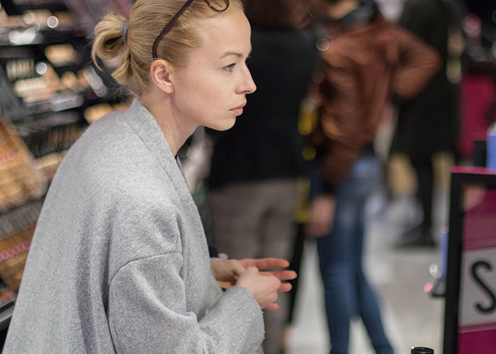 Woman in a store, seemingly considering brands, surrounded by blurred shoppers.