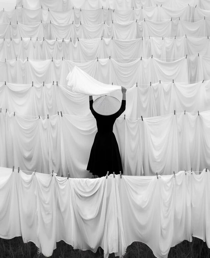 A person in black dress and hat arranging white sheets on a clothesline, showcasing perfectly timed street photography.
