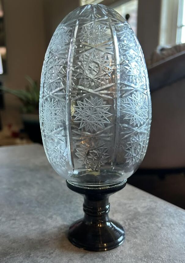 Intricately carved glass egg on a dark pedestal, an unusual thrifting find.