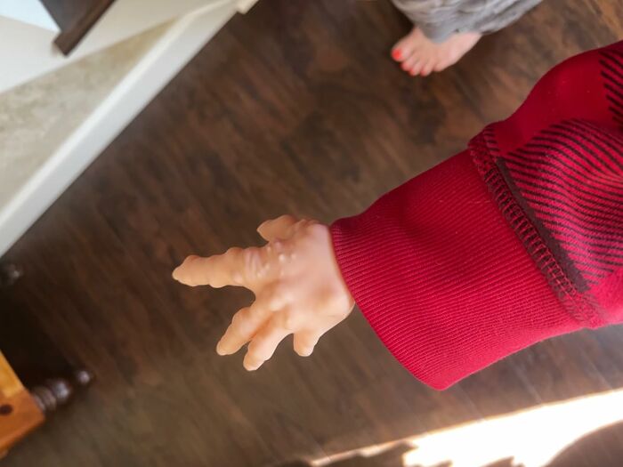 Red sweater with a small, prop hand extending, resting on a wooden floor.