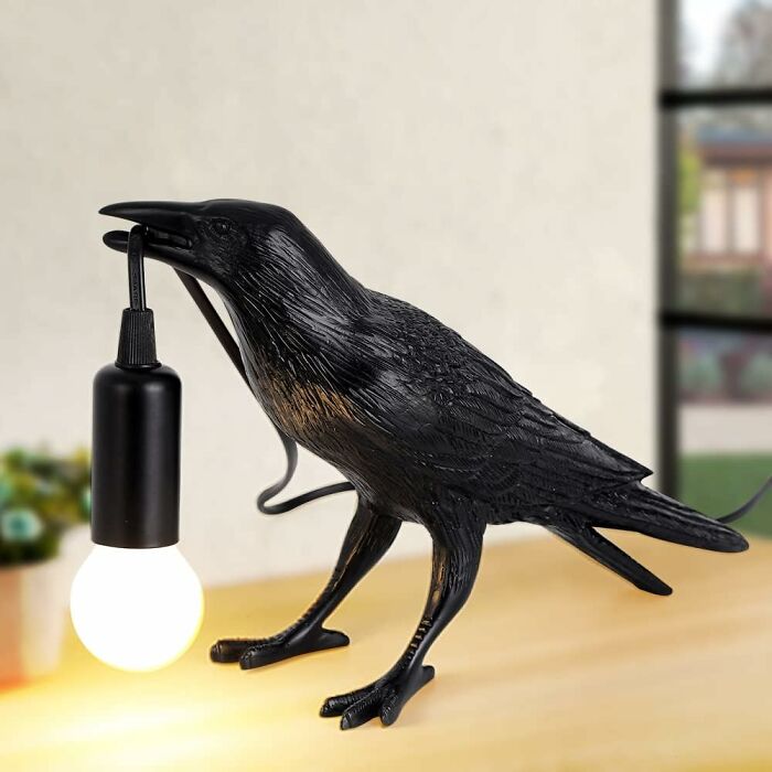 Black crow lamp sculpture holding a light bulb on a table, a show-stopping find for unique home decor.