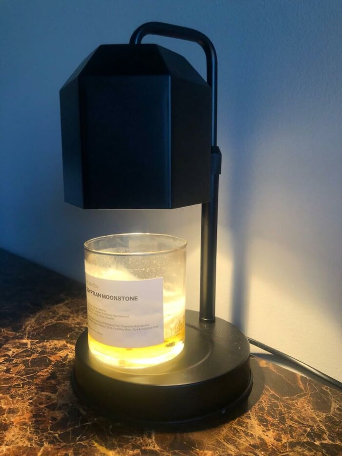 Black candle warmer on marble surface gently melting a scented candle, showcasing useful decor items in a cozy setting.