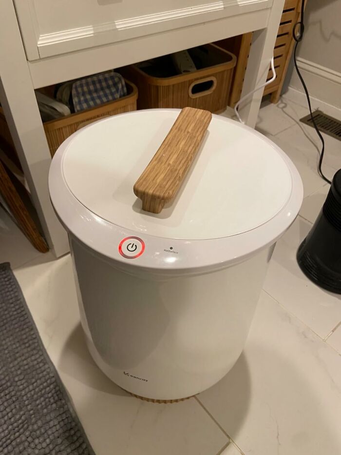 White laundry hamper with a wooden handle in a bathroom, showcasing an ultra-specific product design.