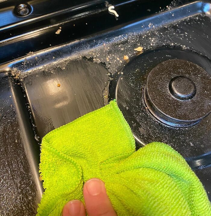 Cleaning a dirty stove with a green cloth, targeting sneaky spots in your home.