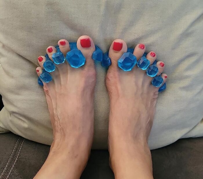 Feet with red nail polish using blue toe separators.