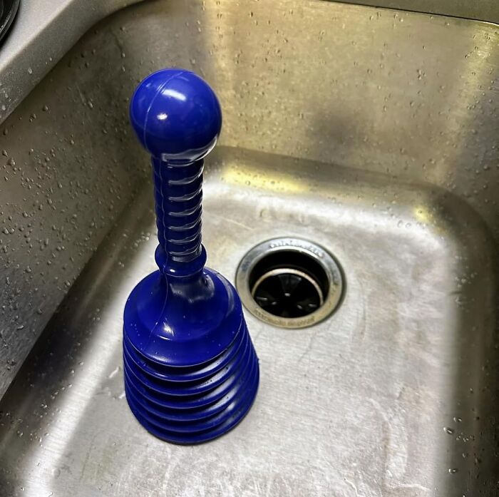 Blue sink plunger as an effective cheapskate alternative in a stainless steel kitchen sink.