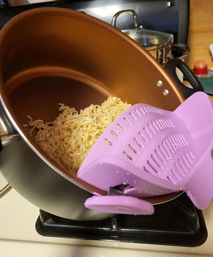 Purple strainer solving noodle draining problem in a pot, showcasing kitchen efficiency.