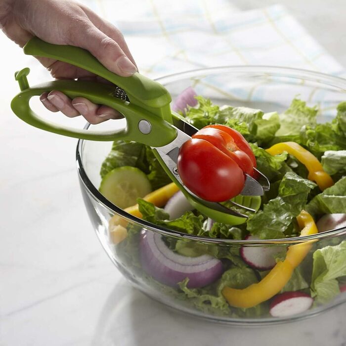 Scissors cutting a tomato over a salad, enhancing a problem-free kitchen life.