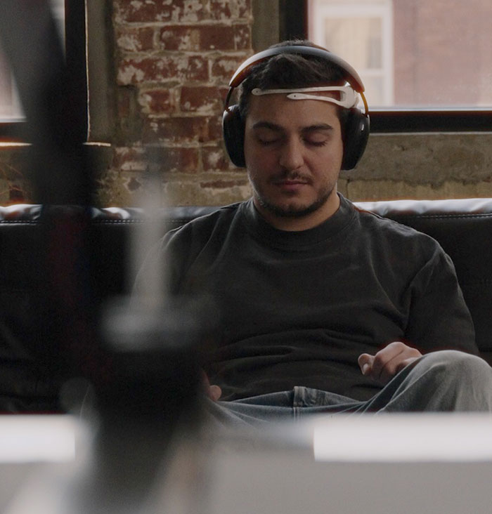 Person wearing headphones, eyes closed, capturing brain activity for unique tattoo imprint by an innovative artist.