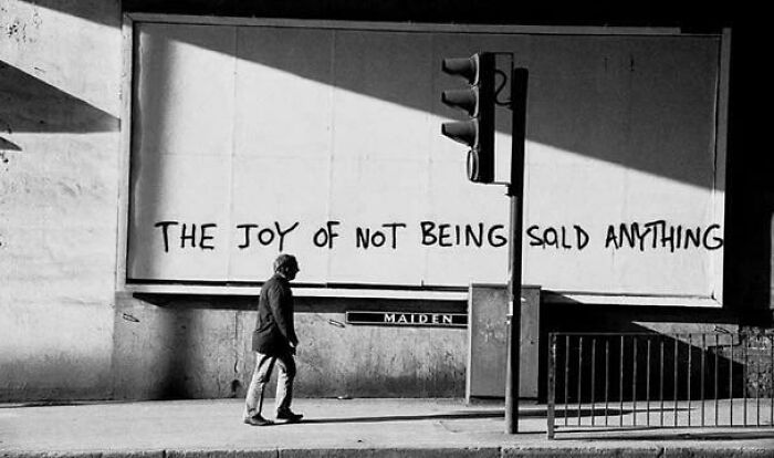 Black and white photo showing street art with the phrase the joy of not being sold anything, highlighting consumerism issues.