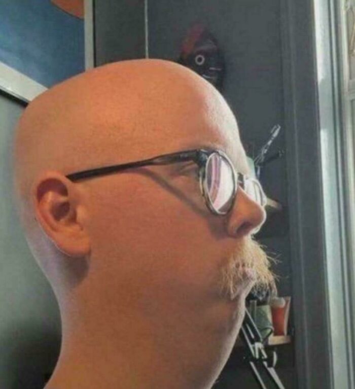 A bald man with round glasses and a long, pointed mustache, representing unfortunate haircuts.