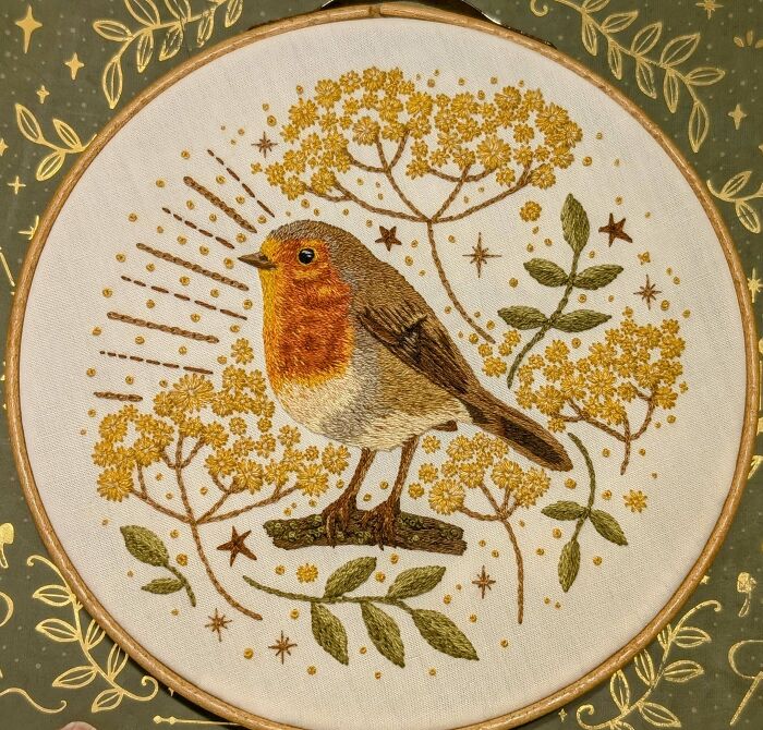 Embroidered bird with orange chest surrounded by yellow flowers and green leaves in detailed embroidery artwork.