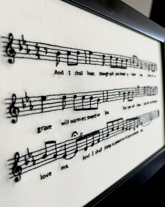 Close-up of a framed embroidery artwork featuring musical notes and lyrics showcasing beautiful embroidery skills.