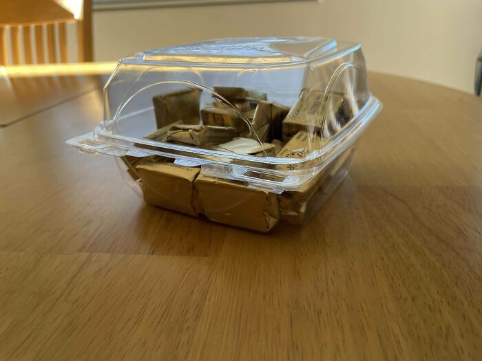 Extra butter packets in a plastic container on a wooden table, showcasing generous customer request fulfillment by food workers.