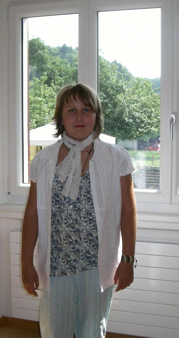 Teen posing indoors in a floral shirt, white vest, and lace scarf, part of people's regrettable past photos that cause cringe.