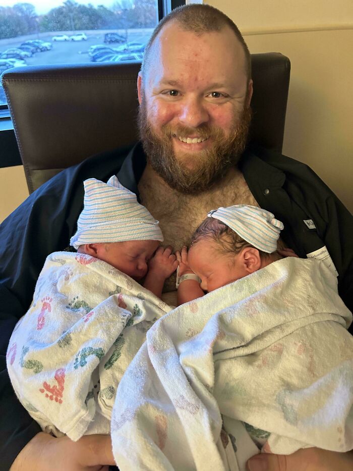 Smiling dad holding and bonding with newborn twins wrapped in blankets, showcasing wholesome parenting moments.