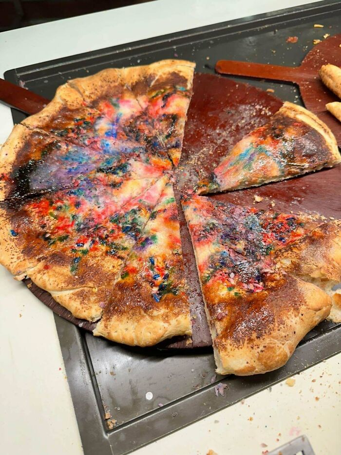 Burnt pizza with unusual colorful toppings on a wooden tray, one slice partially removed, showing a bizarre dish from stupid dishes.