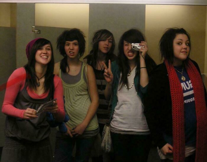 Group of five friends in early 2000s fashion taking a bathroom mirror selfie, capturing a regrettable past moment.