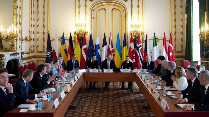 International leaders in a formal meeting room with flags, possibly discussing global policies and decisions.