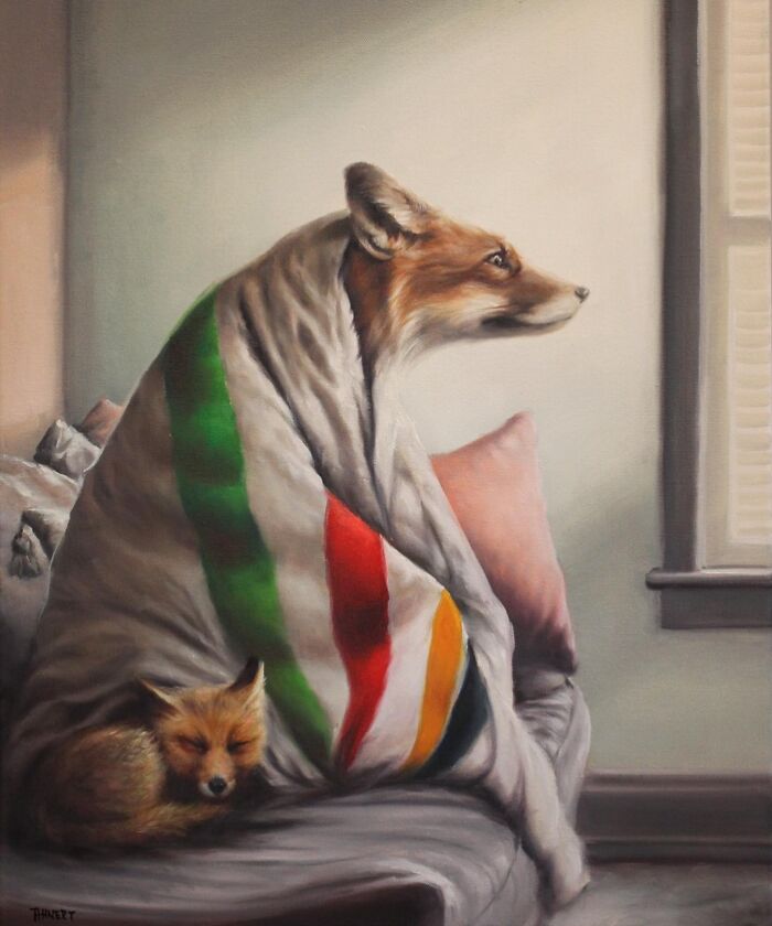 Fox wrapped in a striped blanket, sitting like a person, looking out a window, with another fox resting beside it.