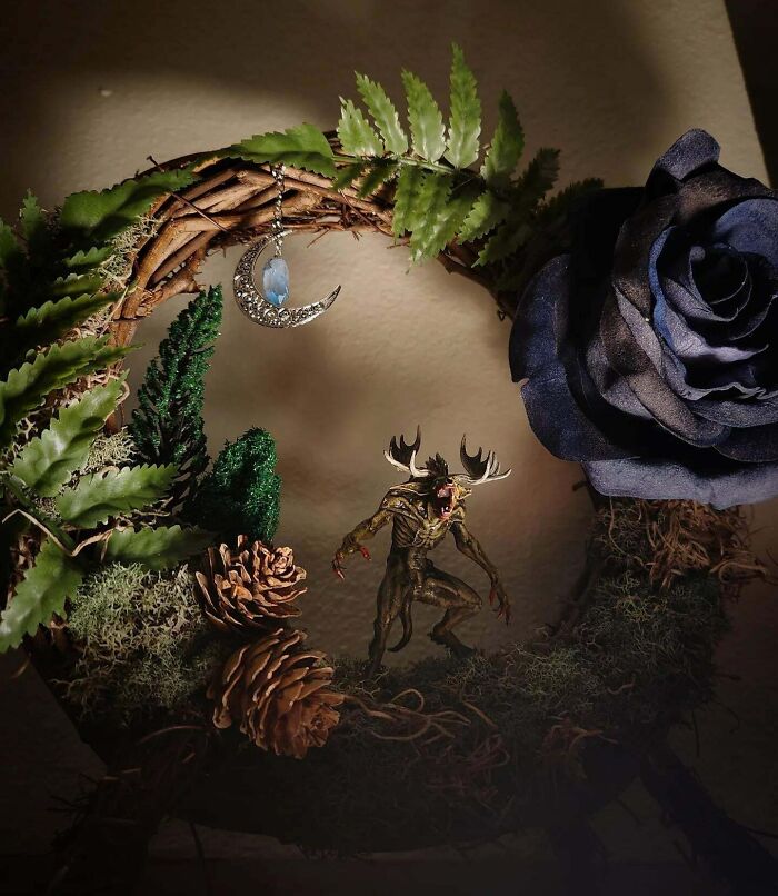 Creepy handmade craft featuring a wreath with a creature, foliage, pinecones, and a celestial pendant.