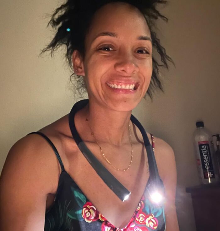 Woman with a neck light smiling, a cheap fix for reading hands-free, wearing a floral top.