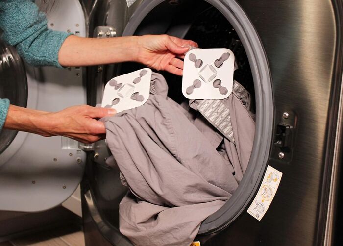 Person placing laundry gadget in a washing machine for a cheap fix to common problems.