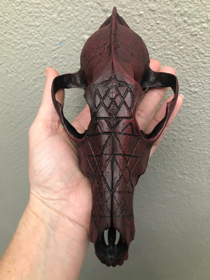 Hand holding a carved, dark red skull, showcasing intricate patterns. Perfect example of interesting creepy handmade crafts.