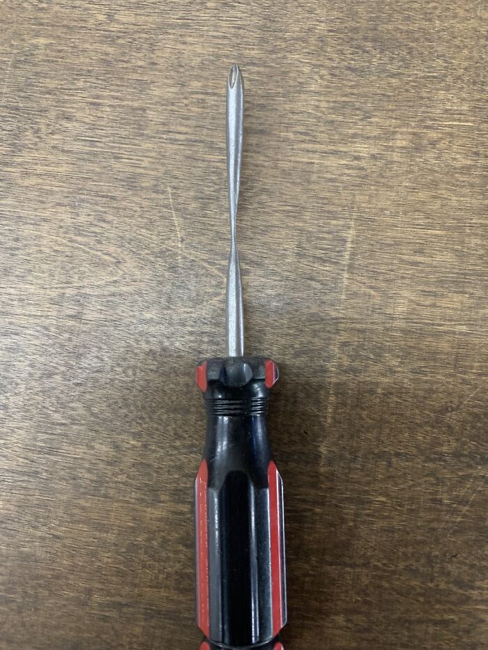 A worn screwdriver on a wooden surface, showcasing its wear over time.