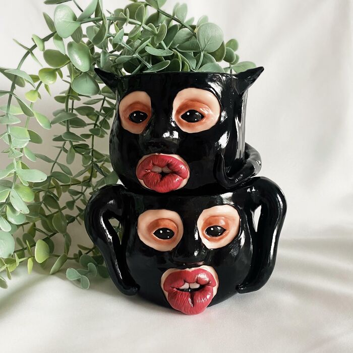 Creepy handmade mugs with expressive faces and plant arrangement.