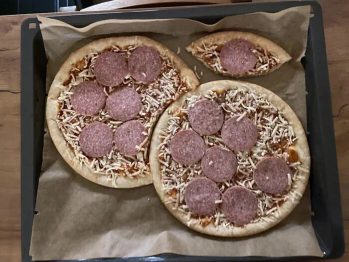 Pizzas asimétricas con salami sobre bandeja de horno, causando sorpresa.