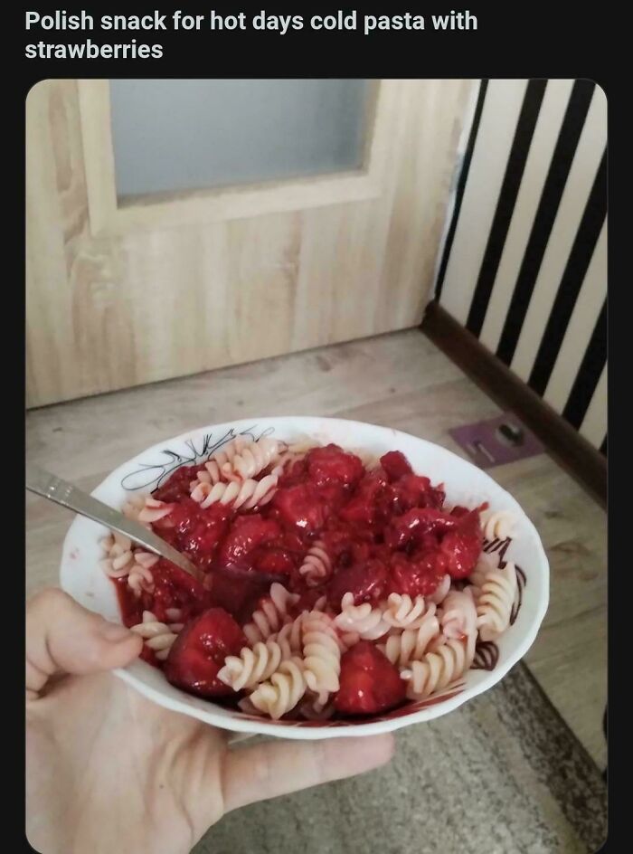 Cold pasta with strawberries in a white bowl held by hand, unique dish combination.