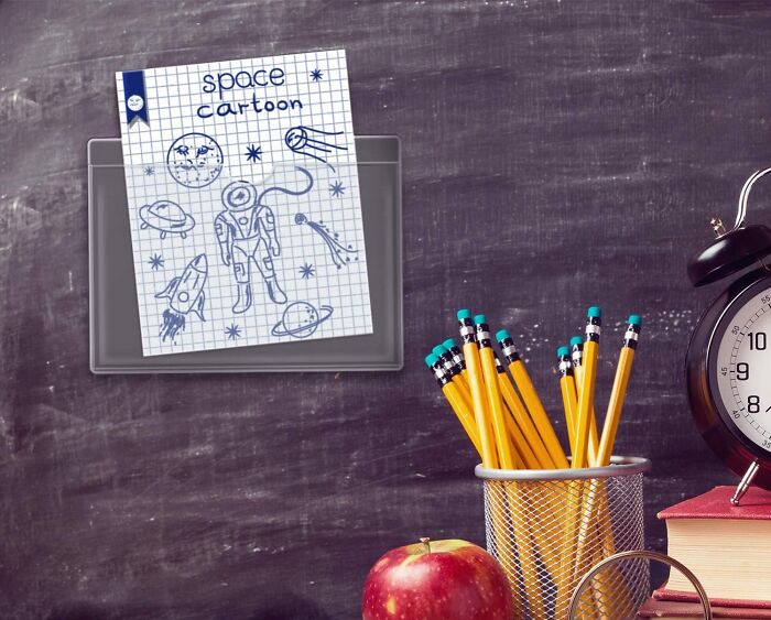 Space cartoon drawing pinned on chalkboard, with pencils, apple, and clock for storing sentimental clutter.