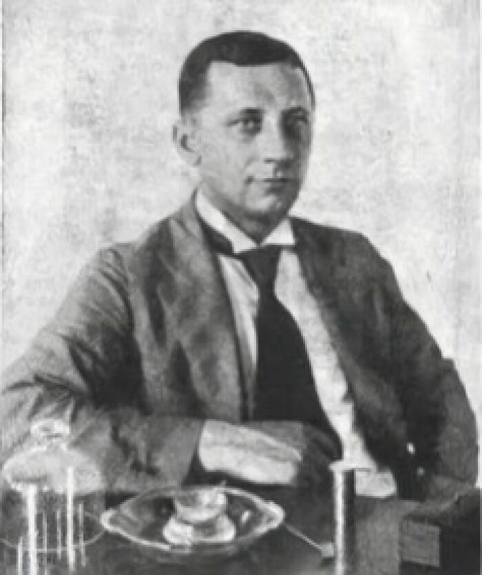 Inventor in formal attire seated at a table with scientific instruments, embodying the theme of inventors and their creations.