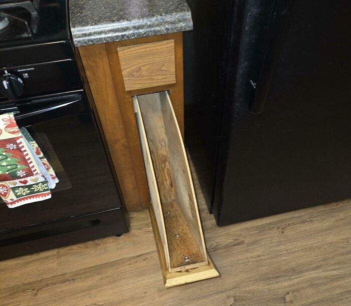 Narrow wooden drawer pulled out from a kitchen cabinet with countertop, showing an unusual design.