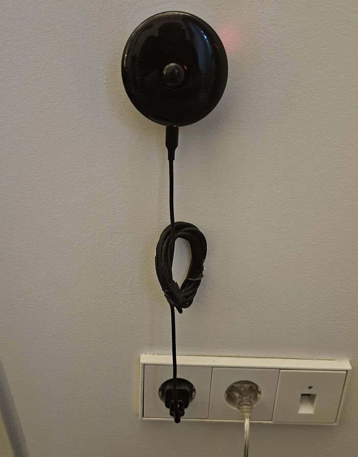 Unusual black device on a wall above an electrical outlet with attached cable, found in everyday settings.