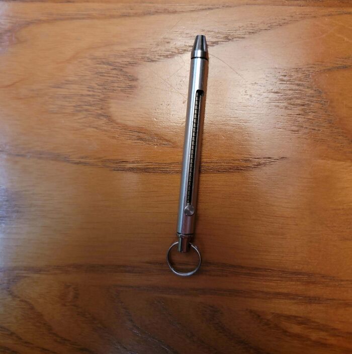 Metallic pen-like device with a ring, unidentified object, placed on a wooden surface.