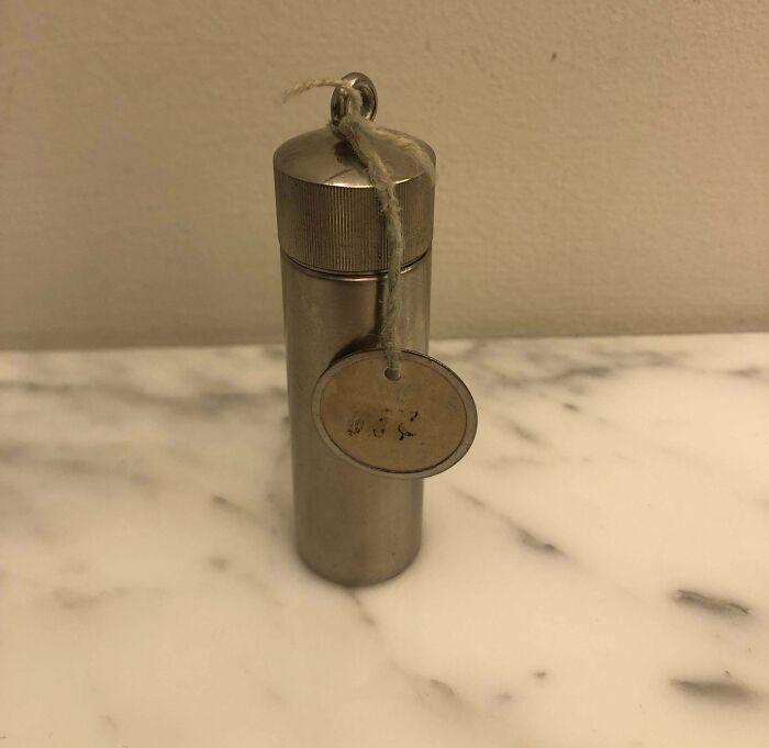 A mysterious metal cylinder with a tag, found on a marble surface.