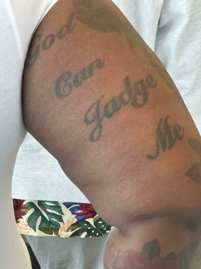 Arm tattoo with the phrase "God Can Judge Me" in cursive script, highlighting unattractive tattoo choices.