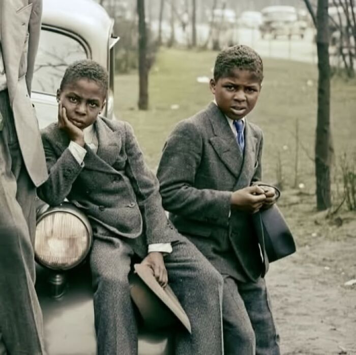 Two young boys in vintage suits, leaning on a car, in a historical photo that continues to resonate today.