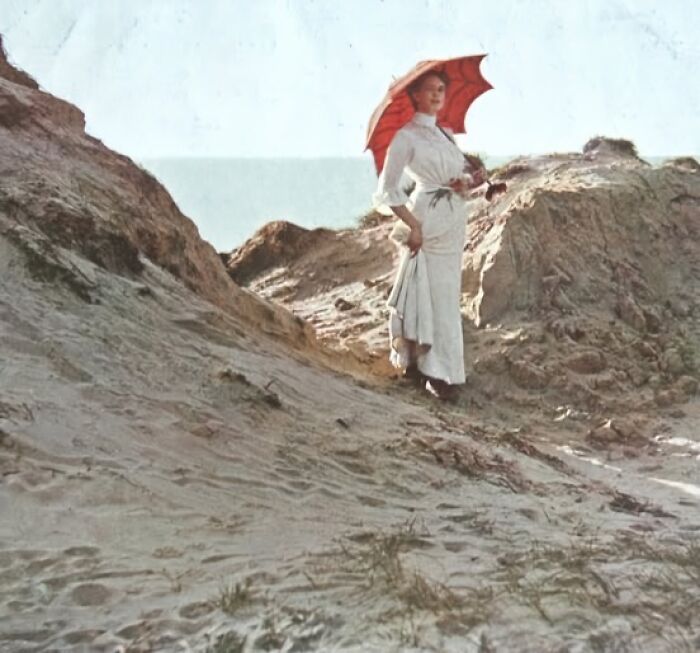 Woman in early 1900s attire holding a parasol on a sandy hill, illustrating historical resonance.