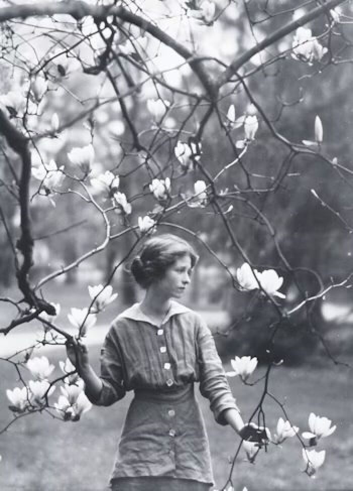Woman standing among blooming branches in a historical black-and-white photo.