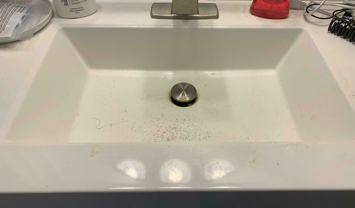 Bathroom sink with design fail showing uneven drainage, with some debris visible around the drain area.
