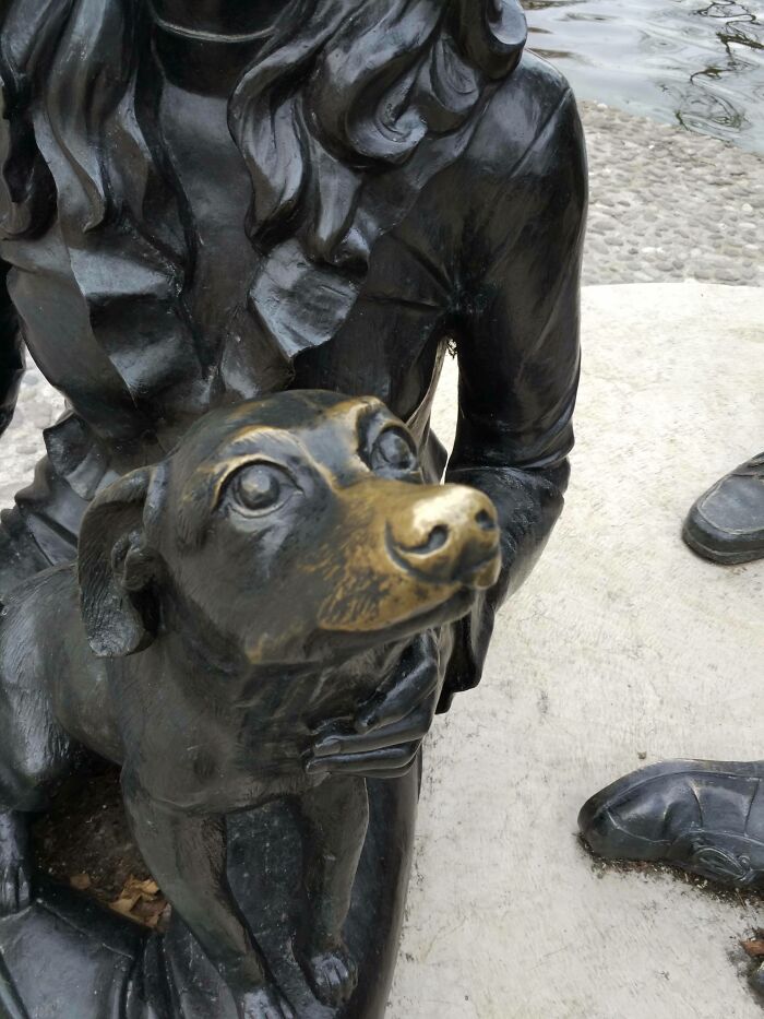 Bronze sculpture of a person holding a dog, displaying wear over time.